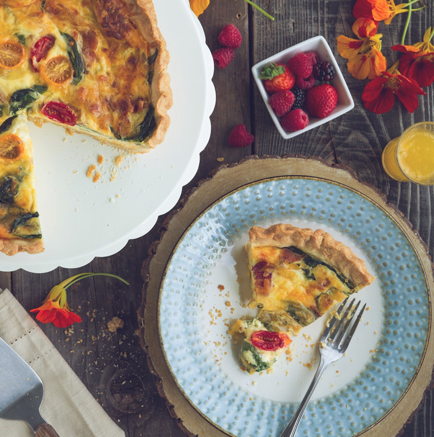 Slice of quiche on a plate with berries in a bowl